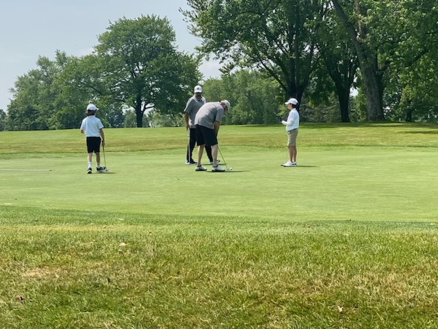 Two young golfers watching their dads on the putting green
